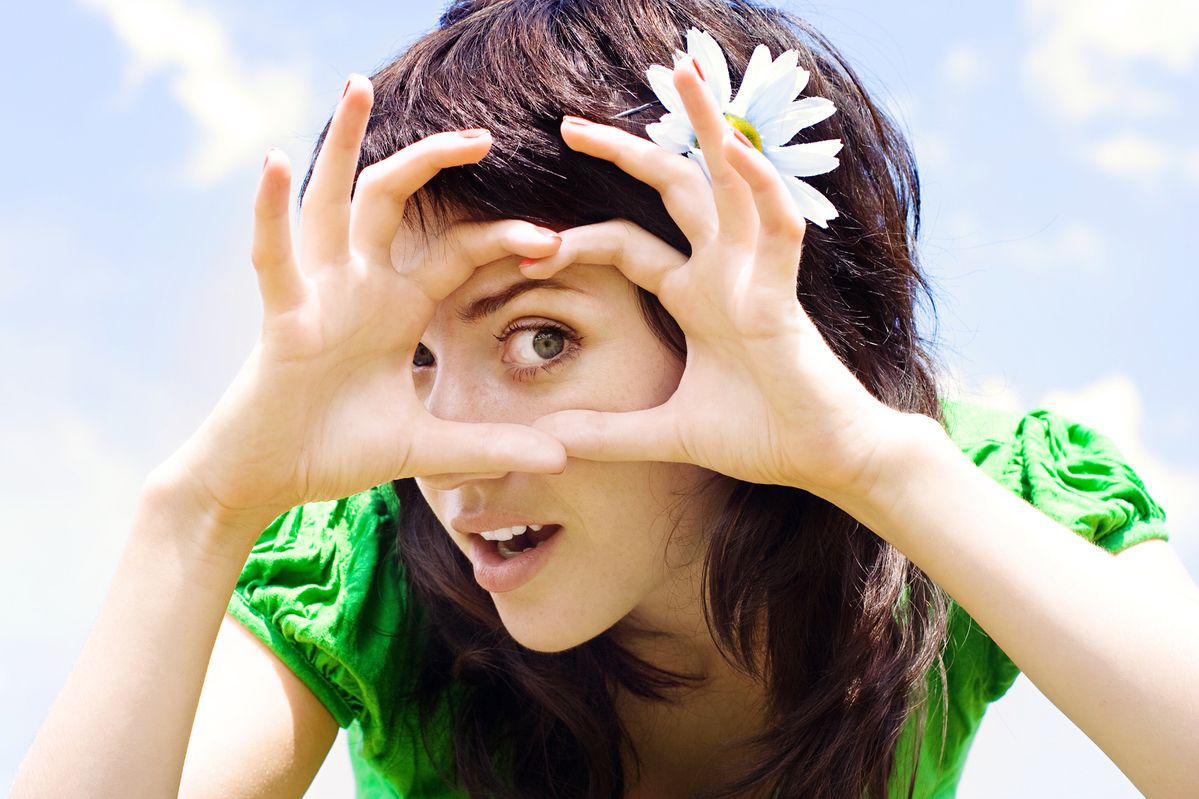 Ein Mädchen mit einer Blume im Haar, das mit ihren Händen ein Herz formt.