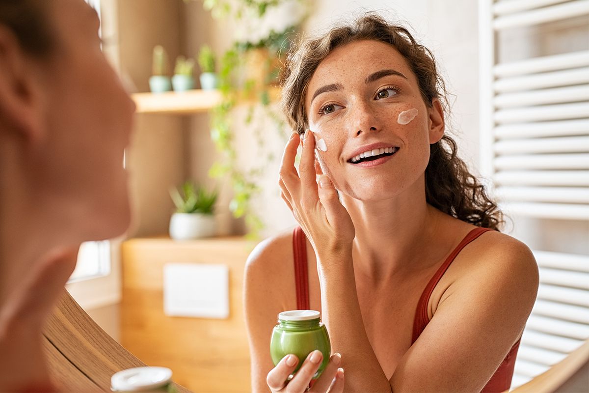 Frau trägt Gesichtscreme im Spiegel