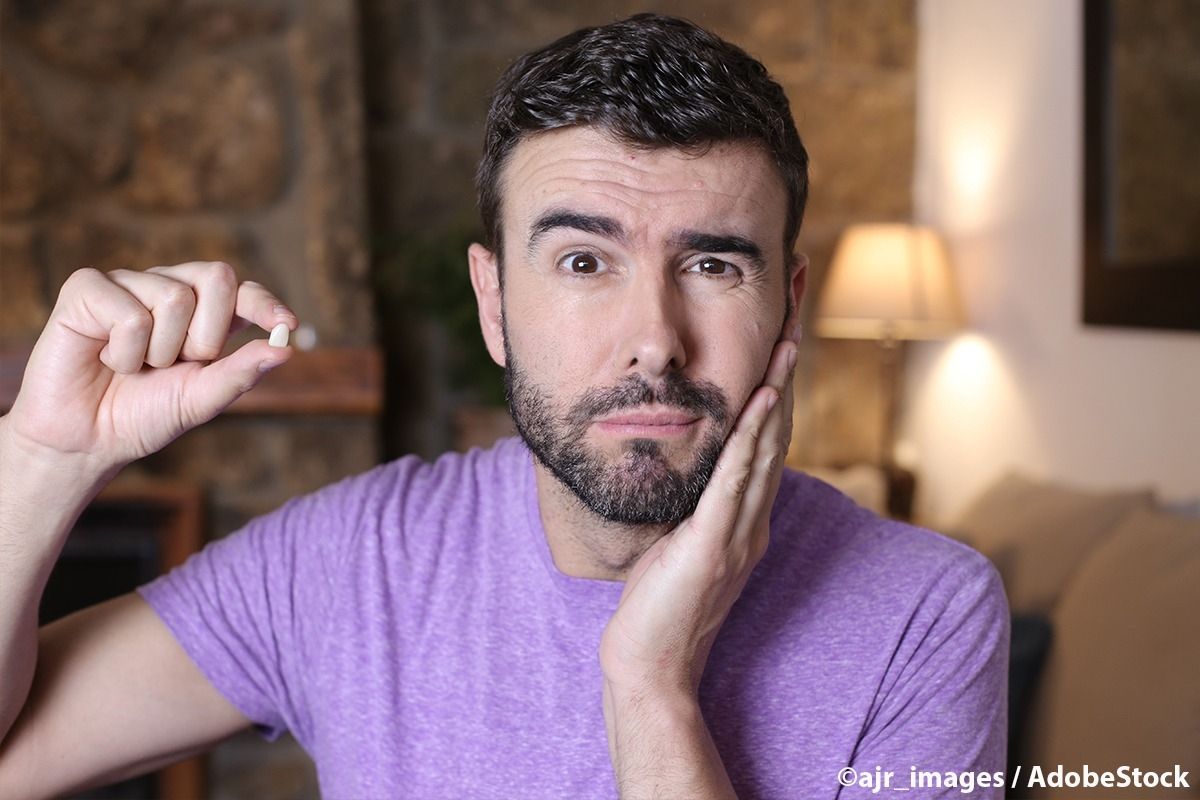 Mann hält eine Zahn hoch und hält sich die Wange.