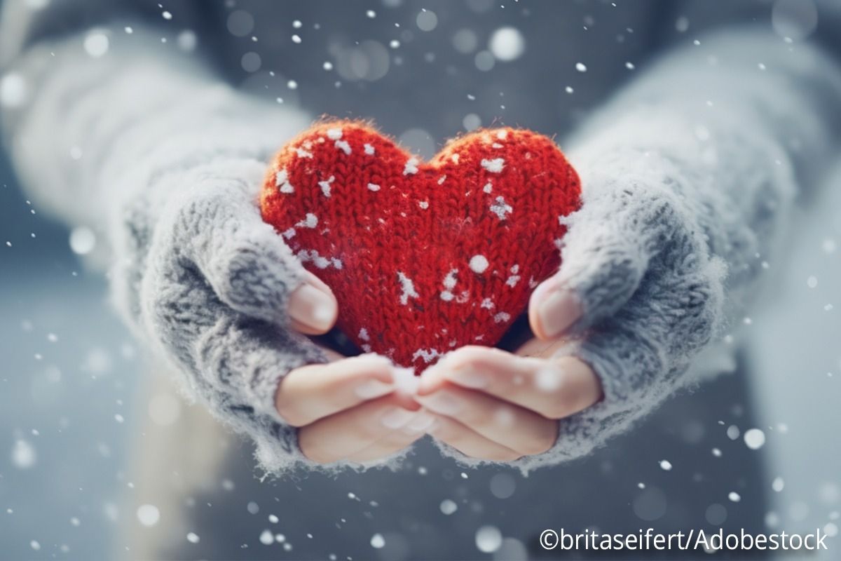 Zwei Hände Zwei Hände in Handschuhen halten ein rotes Strickherz hoch, auf das ein paar Schneeflocken drauffallen.in Handschuhe halten ein grotes Strickherz hoch, wo paar Schneeflocken drauf fallen.