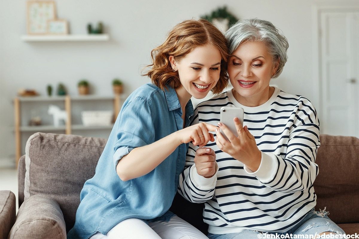 Junge Frau zeigt einer älteren Dame etwas auf einem Smartphone.