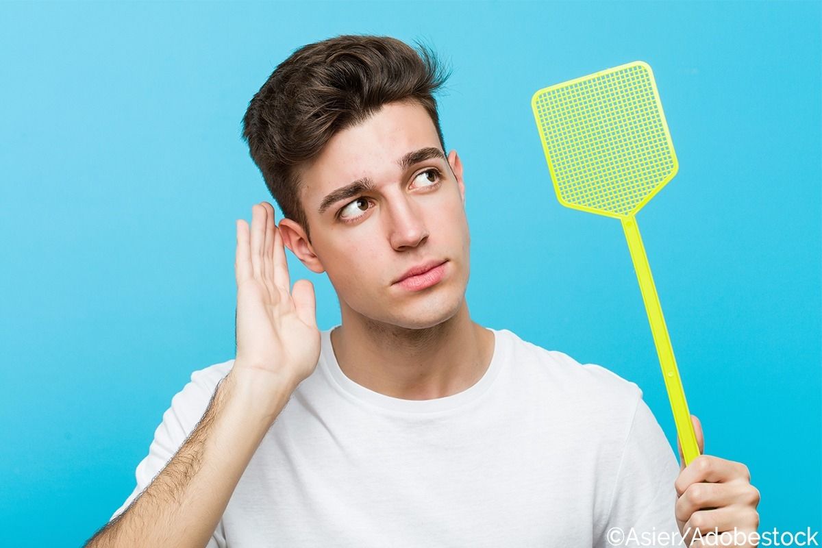 Mann mit einer Fliegenklatsche horcht nach einem Insekt.