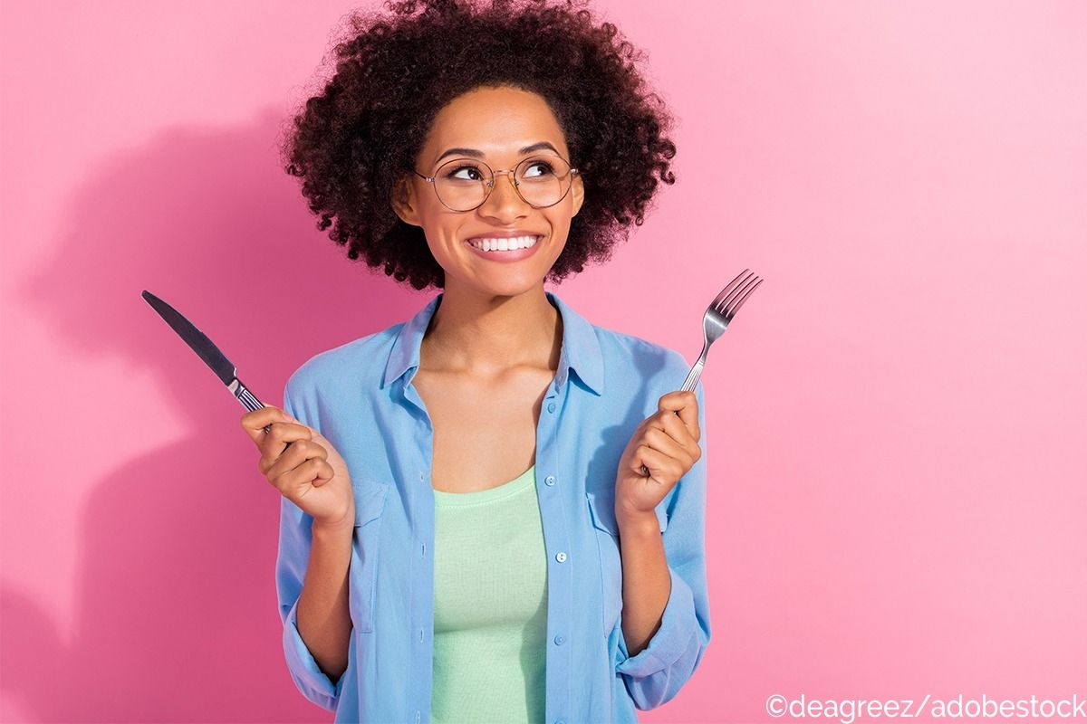 Eine Frau hält ein Messer und eine Gabel hoch, dabei lächelt sie nach oben.