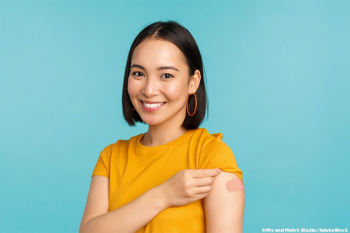 Frau im gelben T-Shirt zeigt ihre Impfstelle.
