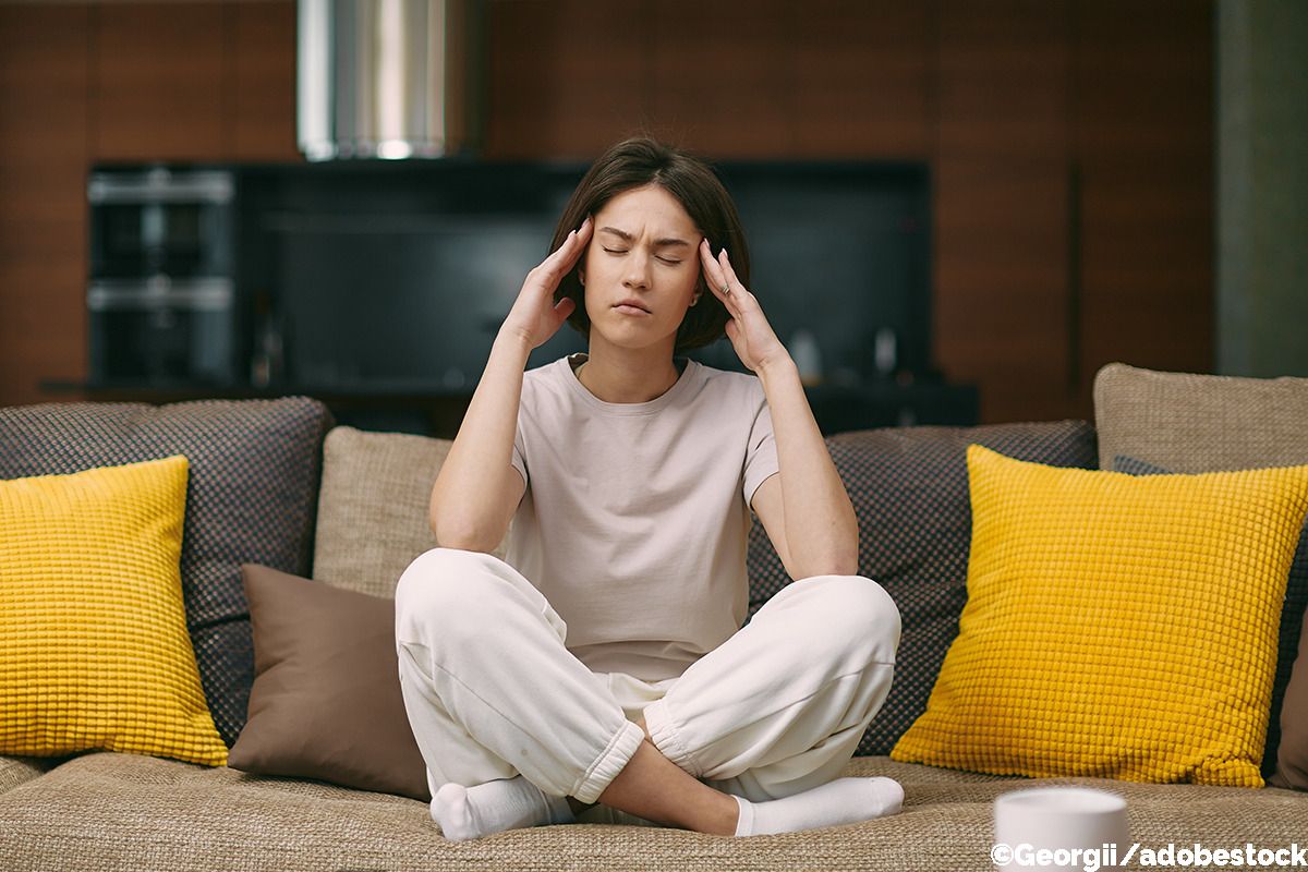 Frau sitzt auf dem Sofa und greift sich an die Schläfen.