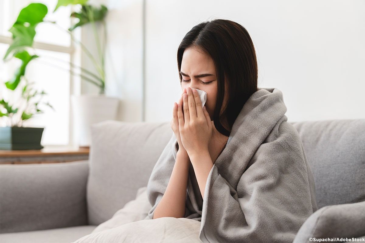 Frau sitzt auf dem Sofa und putzt sich die Nase.