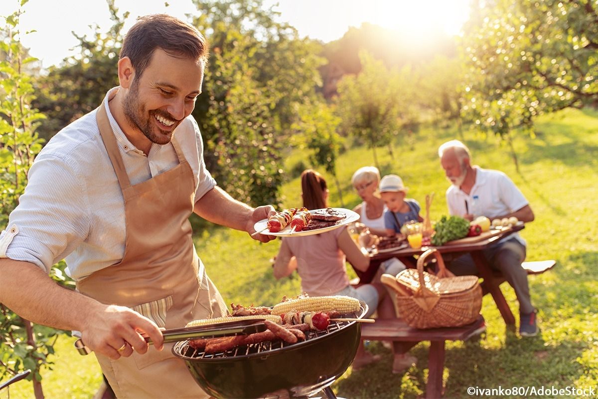Ein Mann grillt und die Familie sitzt am Picknicktisch.
