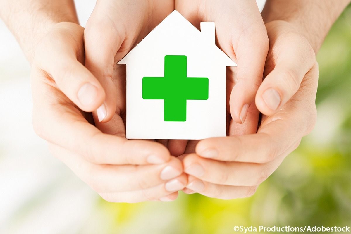 Zwei Handpaare halten gemeinsam ein weißes Haus mit einem grünen Kreuz in der Hand.