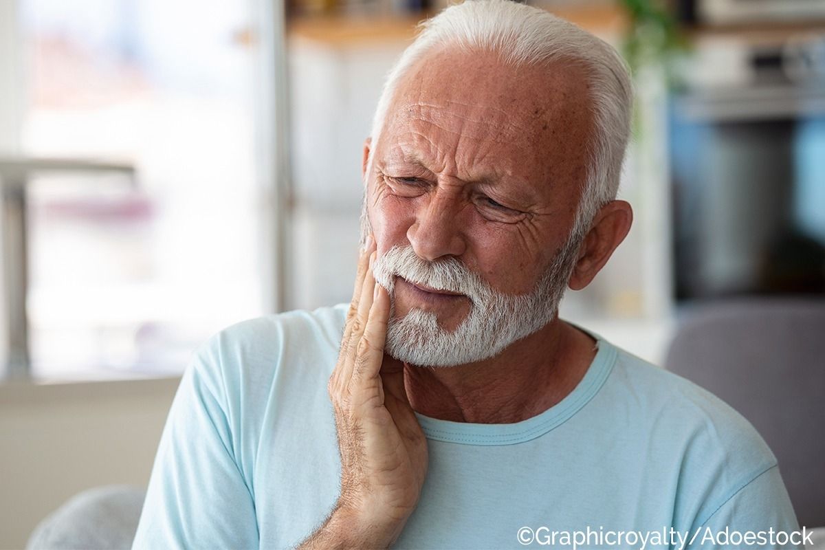 Älterer Mann greift sich an die Wange und hat ein schmerzverzerrtes Gesicht.