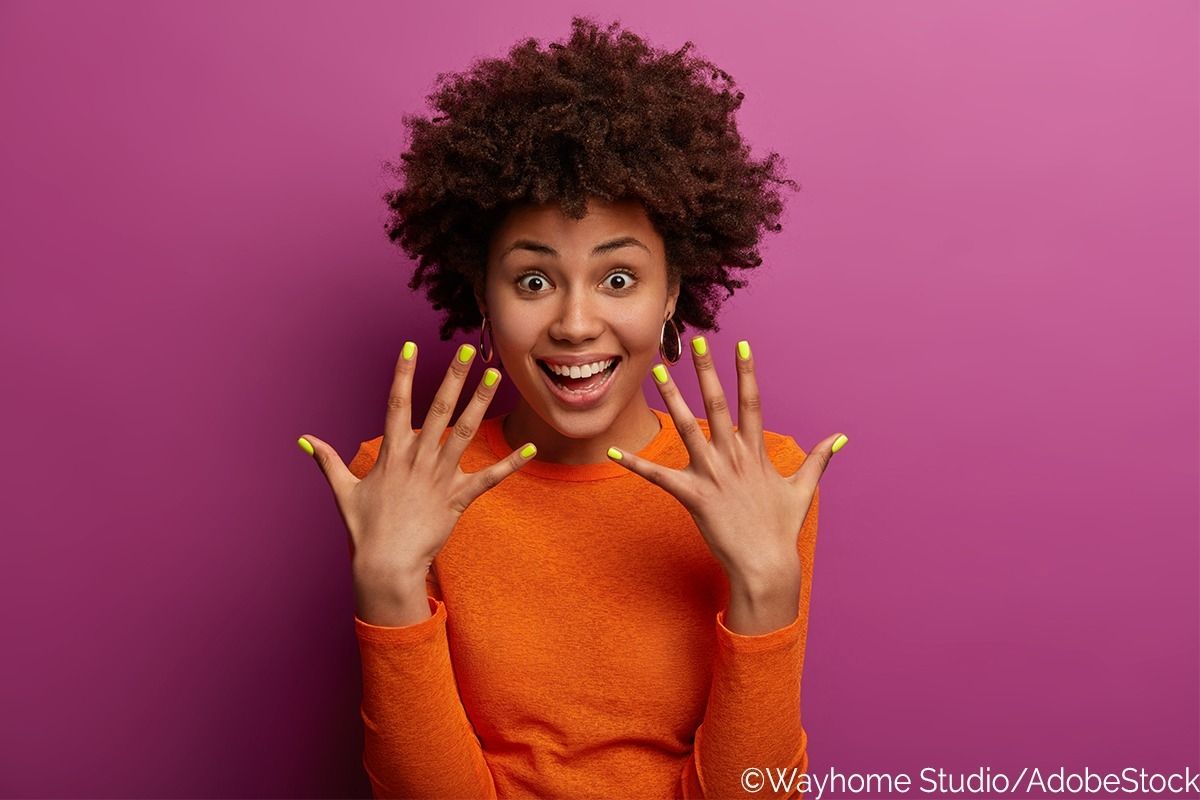 Frau hält vor einer pinken Wand ihre grasgrün lackierten Nägel hoch.