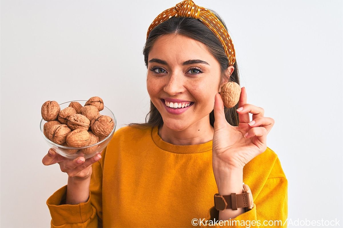 Eine Frau hält mit einer Hand eine Glasschale mit Walnüssen hoch und mit der anderen eine einzelne Walnuss. Zudem lächelt sie in die Kamera.