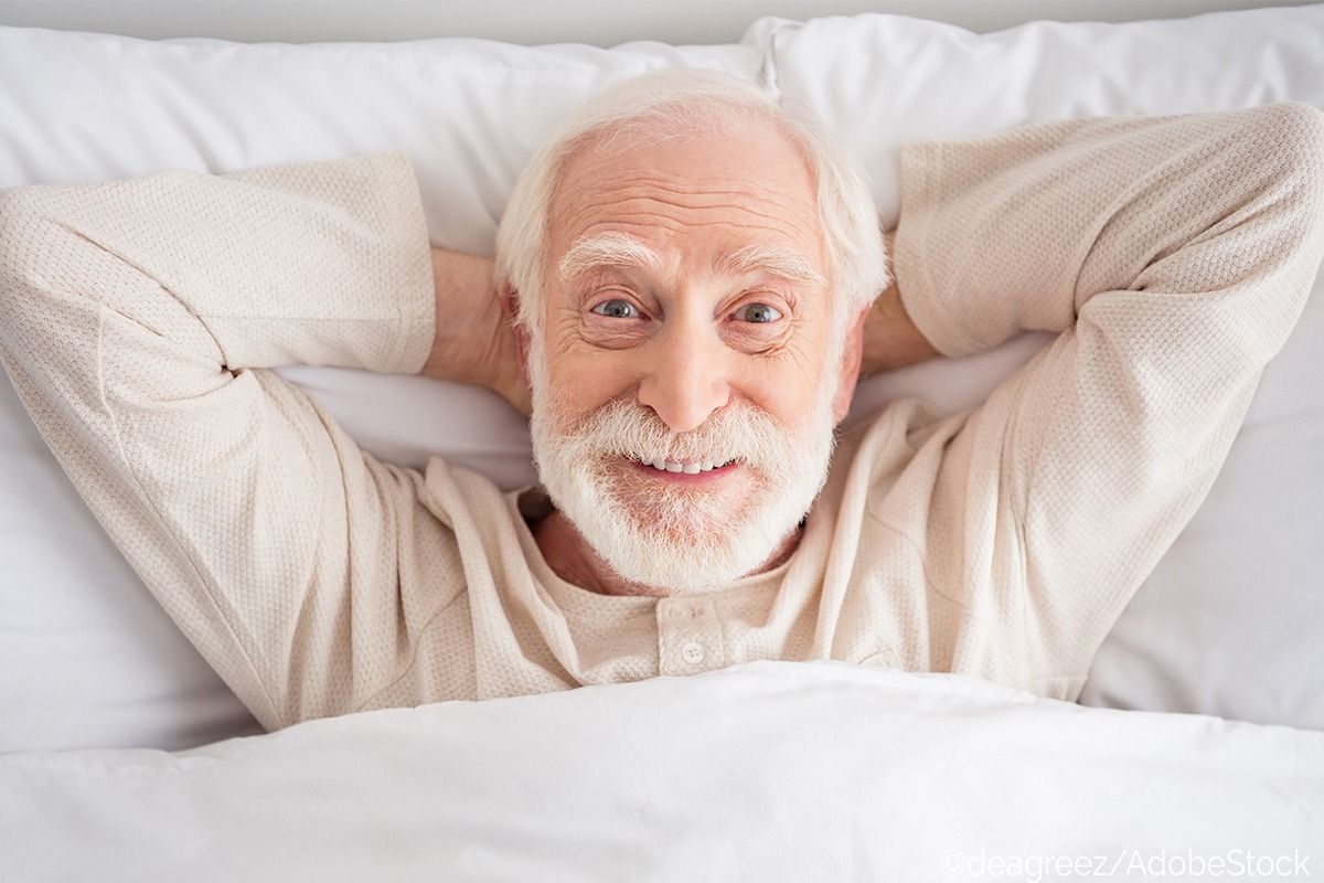 Älterer Mann hat die Hände hinter dem Kopf verschränkt und liegt im Bett