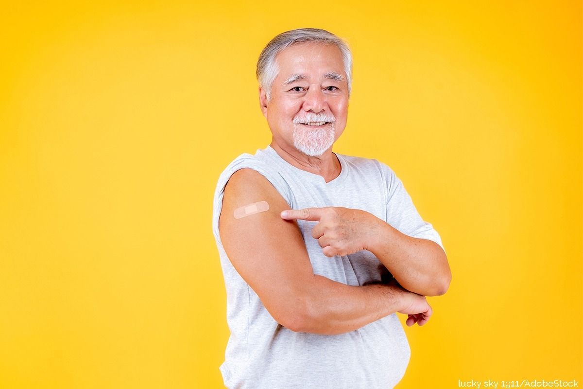 Ein Mann zeigt auf seine Impfstelle und lächelt dabei.