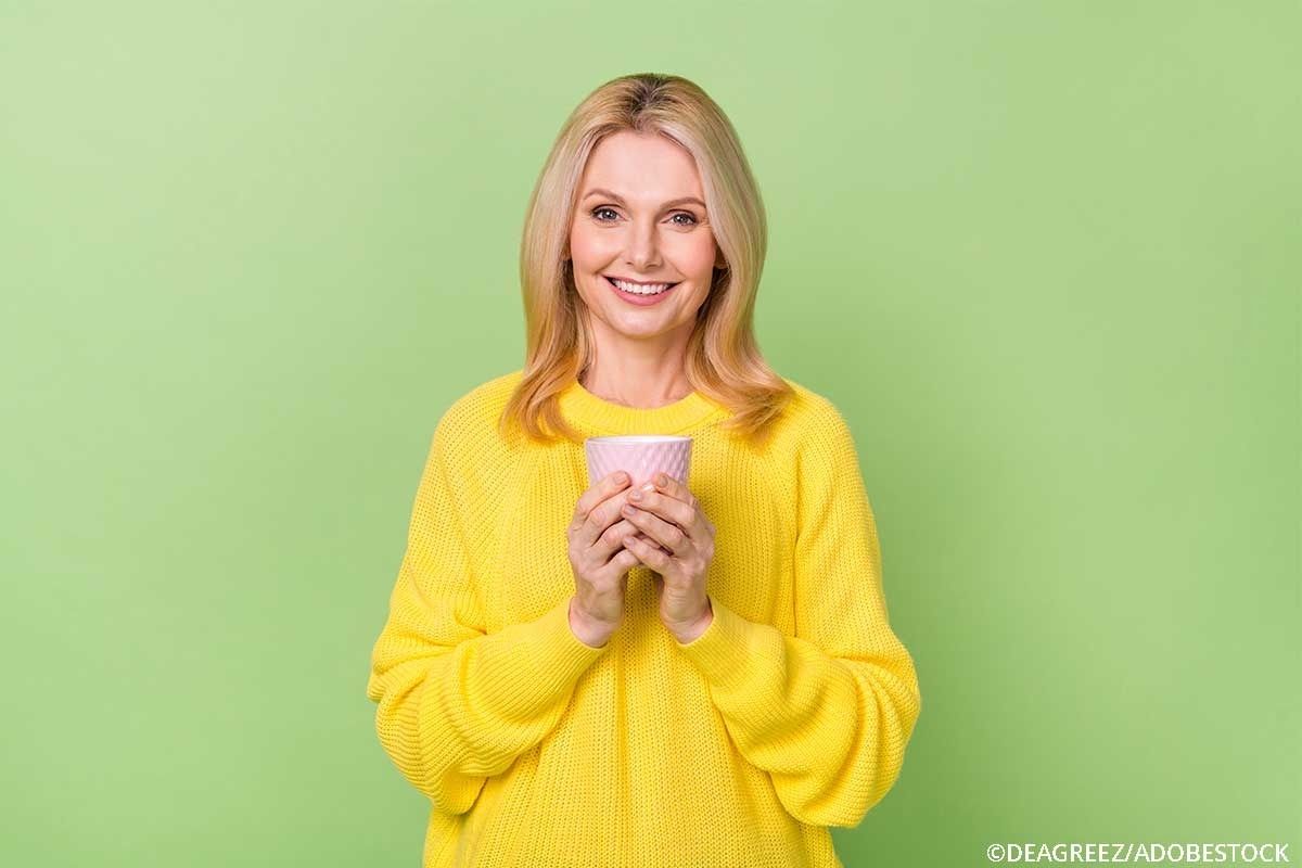 Frau im gelben Pullover hält eine Tasse fest.