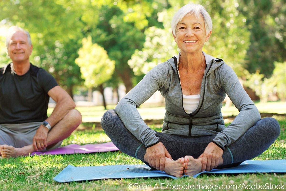 Eine ältere Frau und ein älterer Mann machen auf einer Wiese in Sportsachen Yoga.