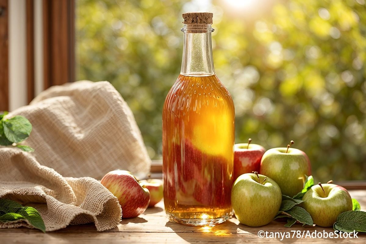 Auf einem Holztisch steht eine Apfelessigflasche aus Glas, umgeben von roten und grünen Äpfeln.