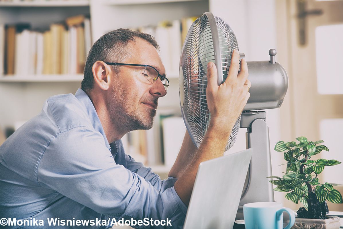 Mann, der sich mit einem Ventilator im Büro abkühlt.