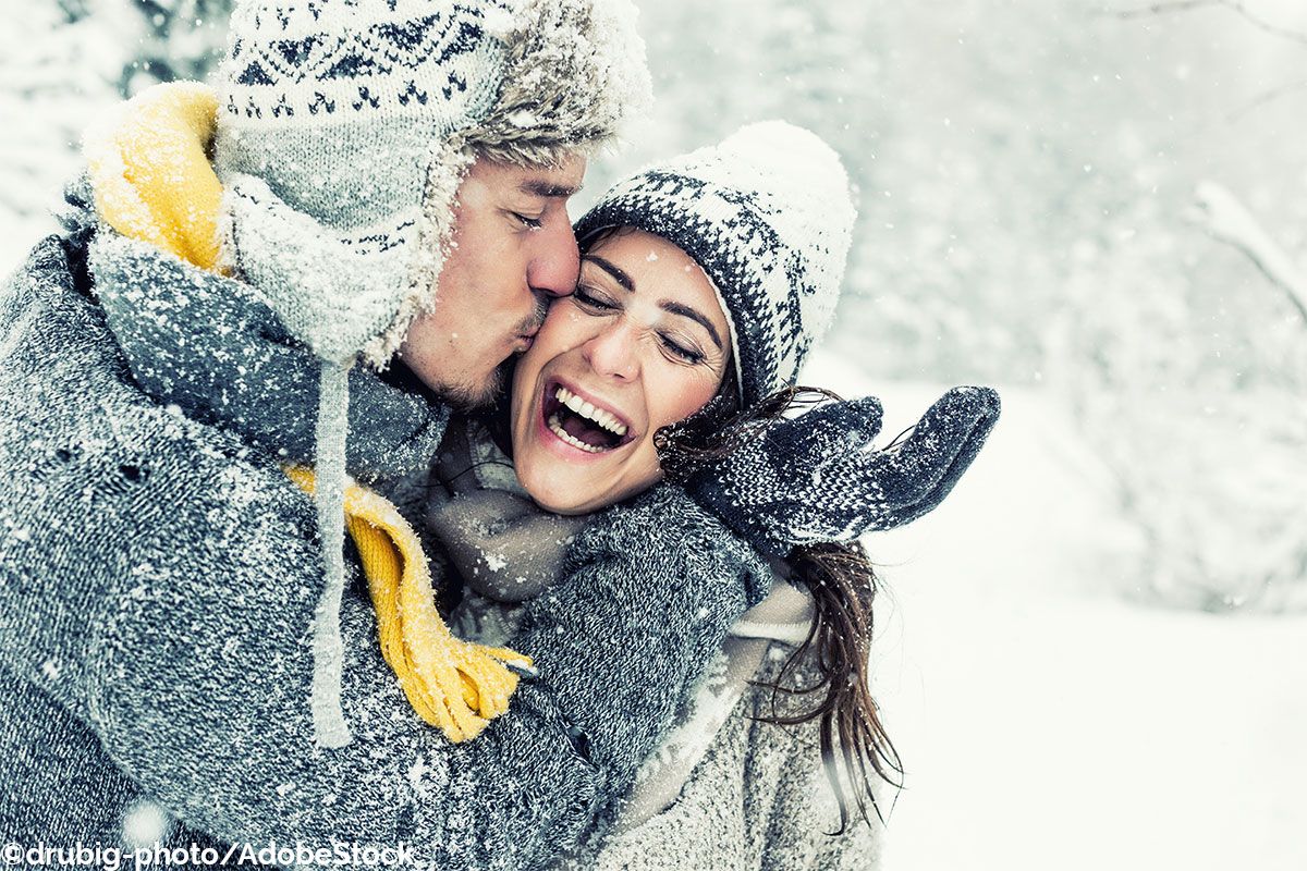 Ein glückliches Paar umarmt sich im Schnee während des Winters